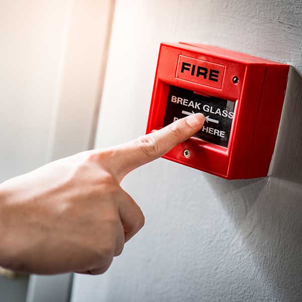 Male hand pointing at red fire alarm switch